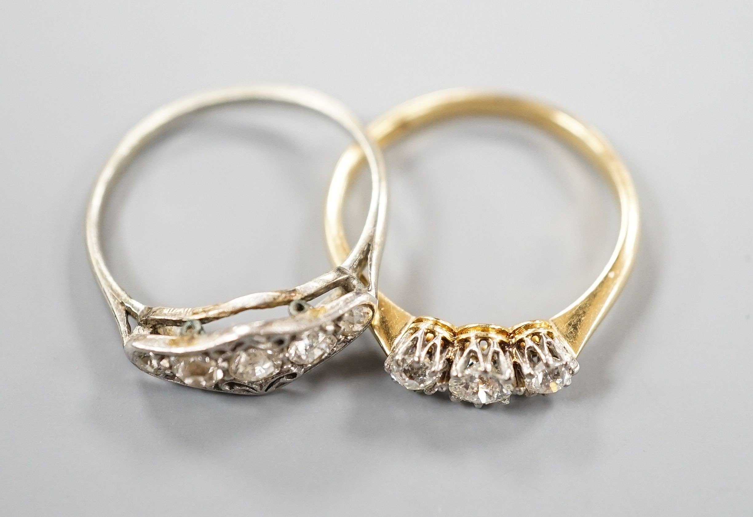 An 18ct and three stone diamond ring, size M and a white metal and graduated five stone diamond set half hoop ring, size M, gross weight 3.8 grams.